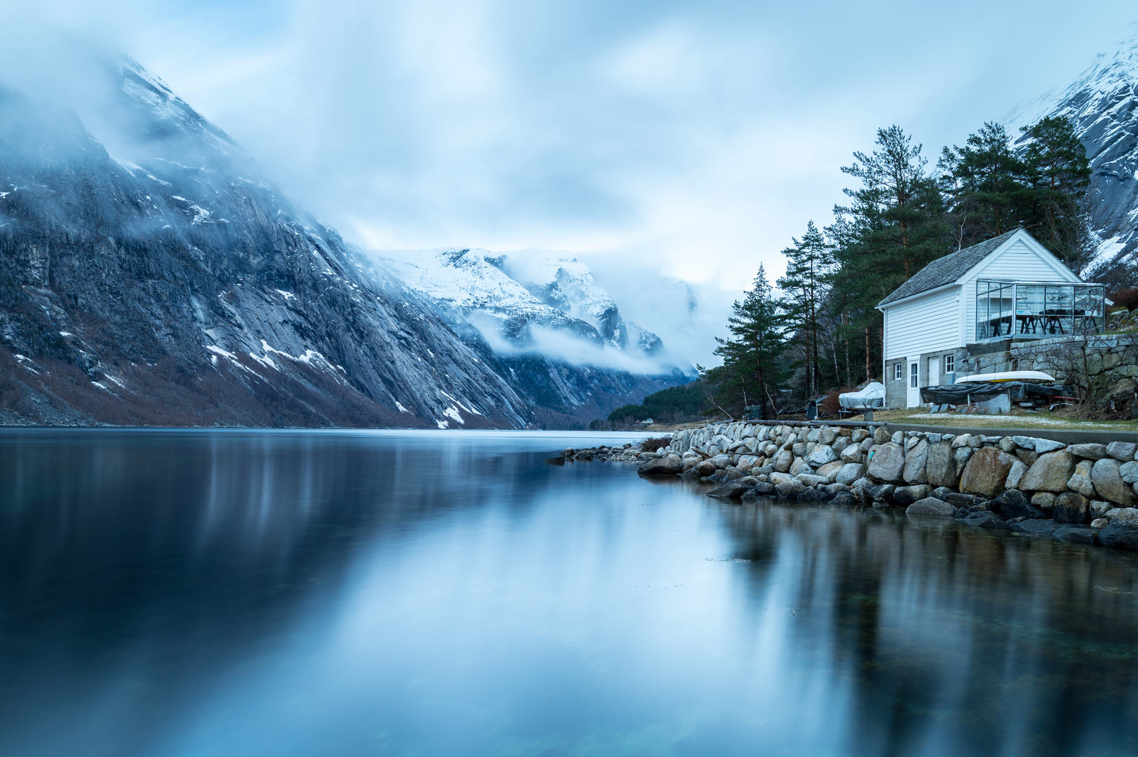 Hütte am Fjord mit Wolken in den Bergen