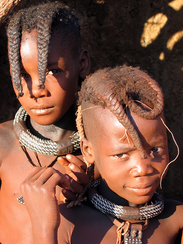 Junge Himba-Mädchen tragen zwei nach vorn stehende Zöpfe