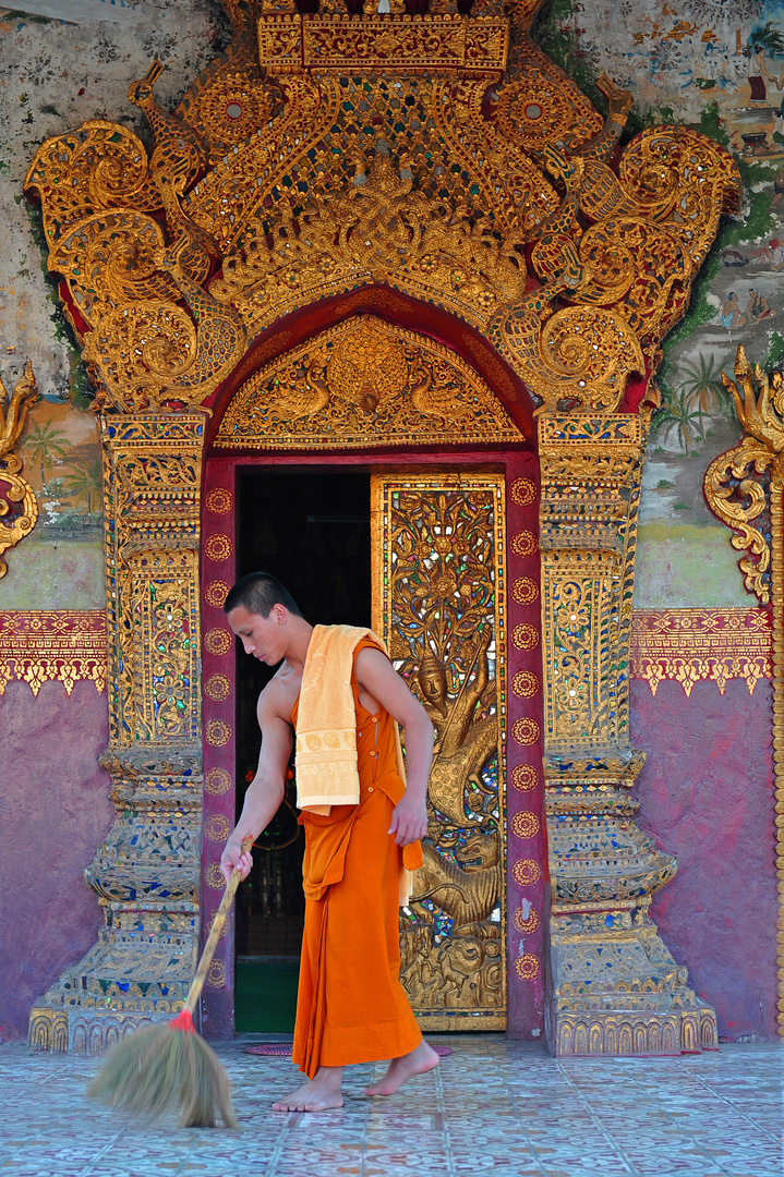 junger Mönch beim Ausüben seiner morgendlichen Pflicht im Dienste seines Klosters in LuangPrabang