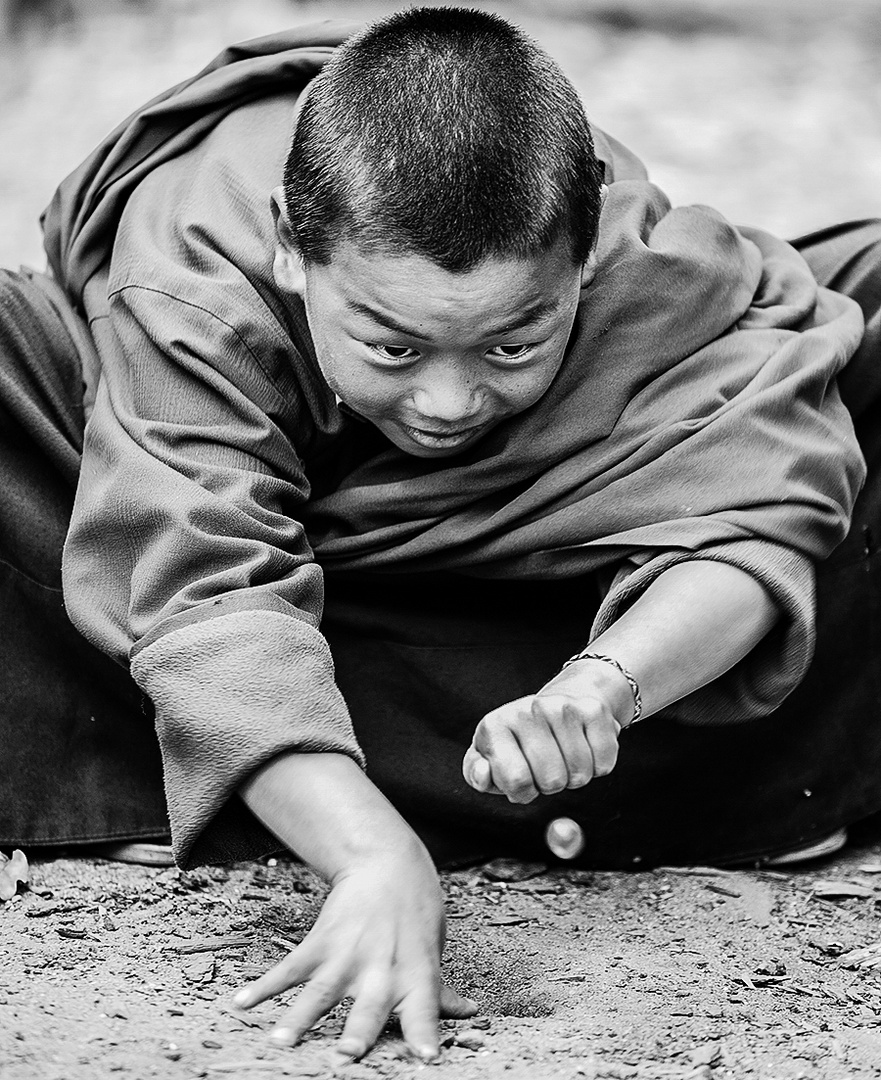 Junger Mönch in Bhutan spielt mit Murmeln