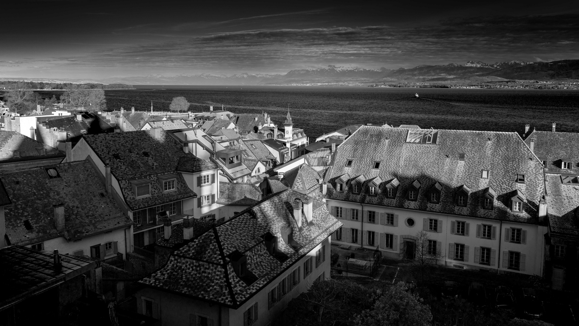 Les toits du bourg de Nyon, le lac Léman et les Alpes.