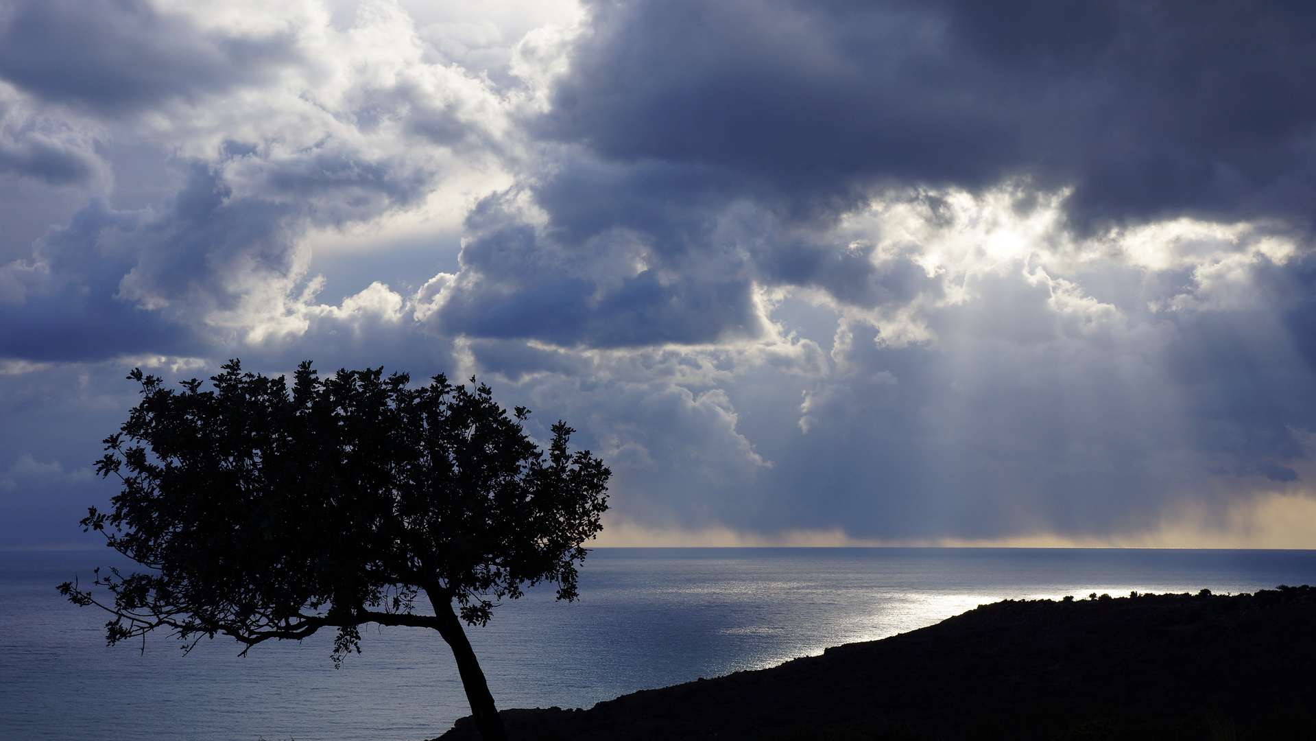 Licht strahlt durch dunkle Regenwolken über dem Meer