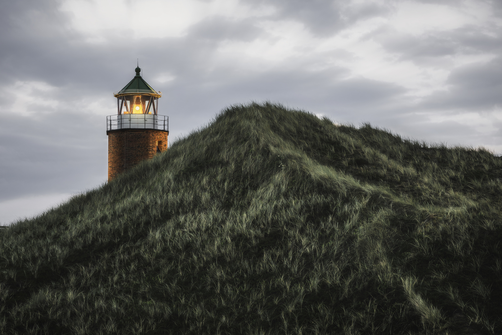 Lit lighthouse on a hill with tall grass and moss on Sylt island