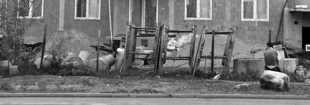 Lodz in Polen. Ein Obdachloser sitzt auf einem Stein vor einer Baustelle einer zukünftigen Siedlung