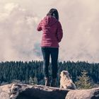 Millennial girl and her dog on mountain rocks looking in the distance