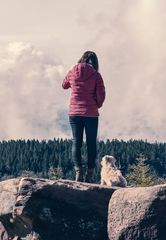 Millennial girl and her dog on mountain rocks looking in the distance