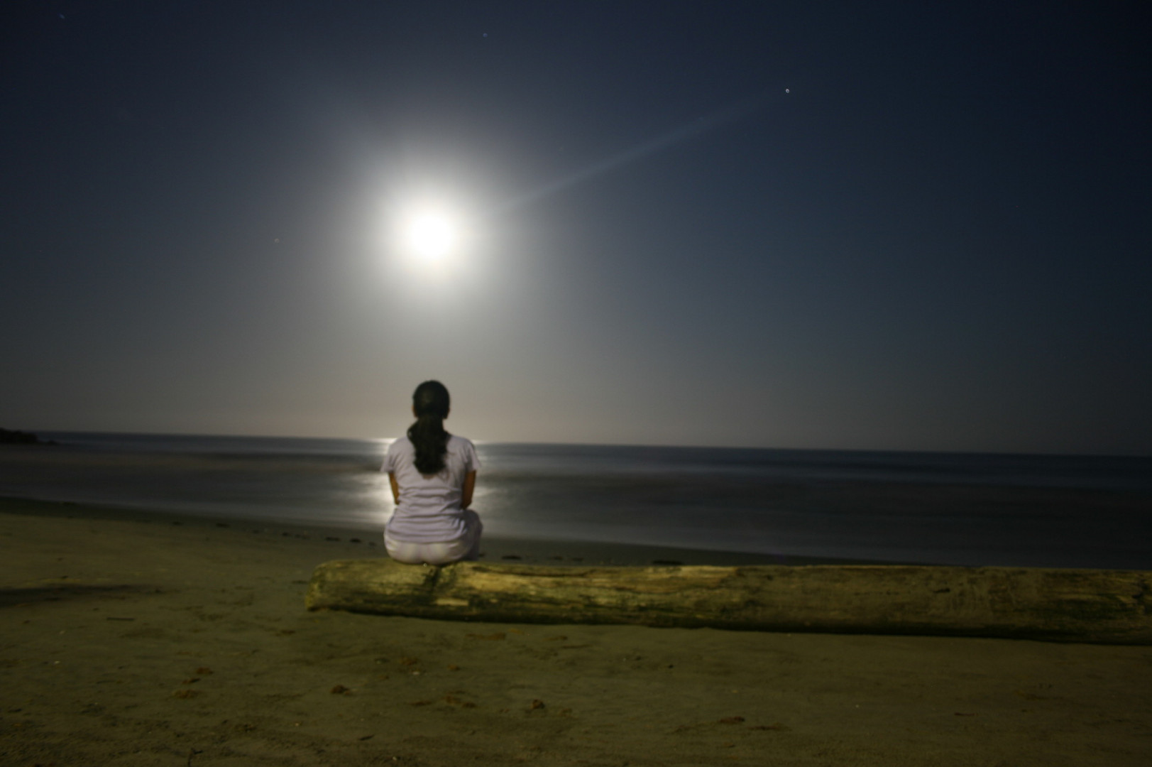 Mujer sentada en la playa viendo la luna