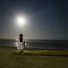 Mujer sentada en la playa viendo la luna