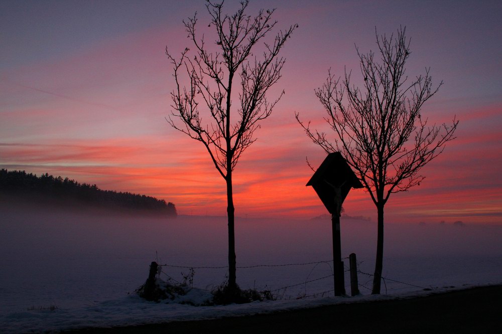 Nebel über Schneefeld mit Feldkreuz nach Sonnenuntergang