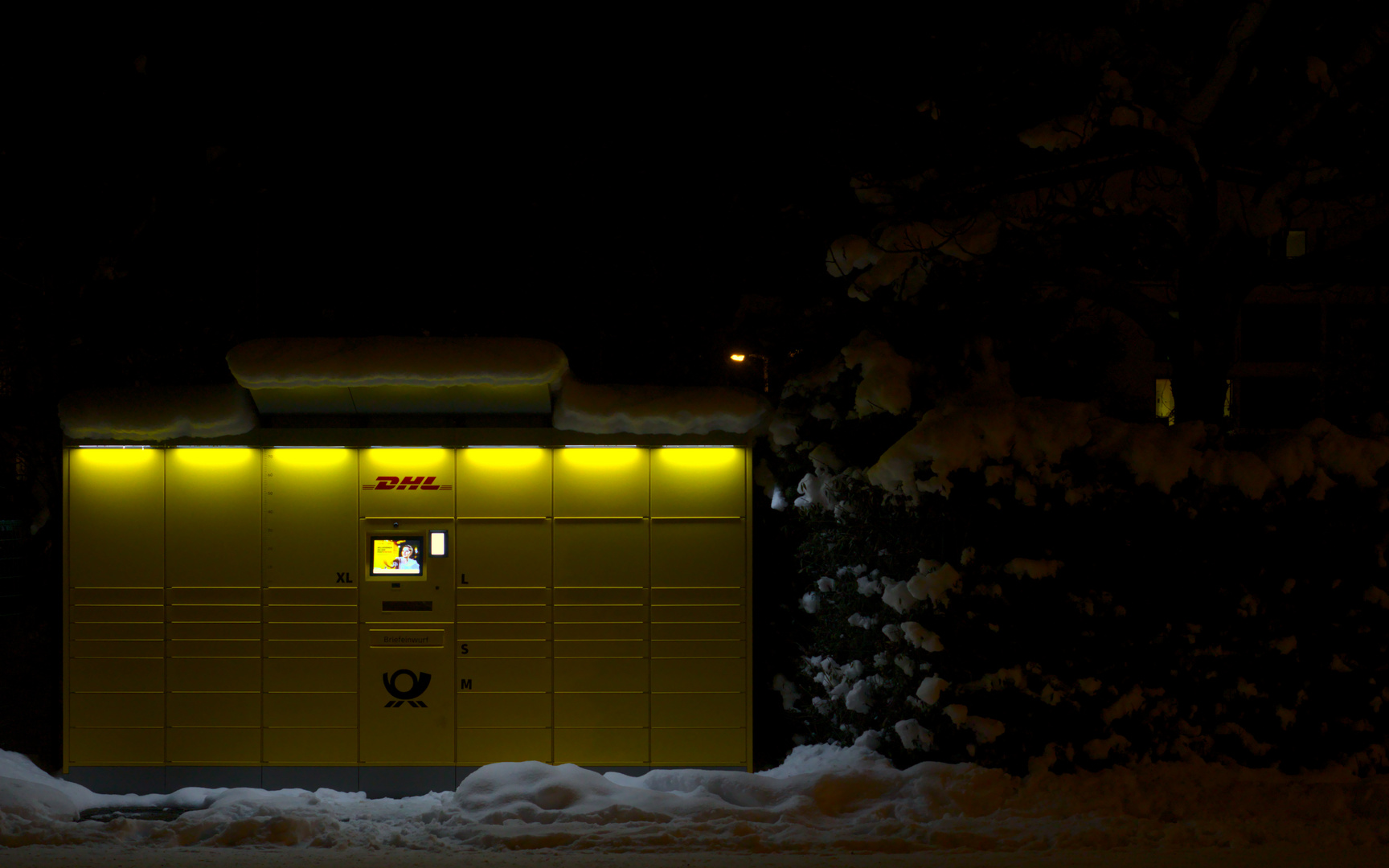 Packstation in verschneiter Mittelstadt bei Dunkelheit