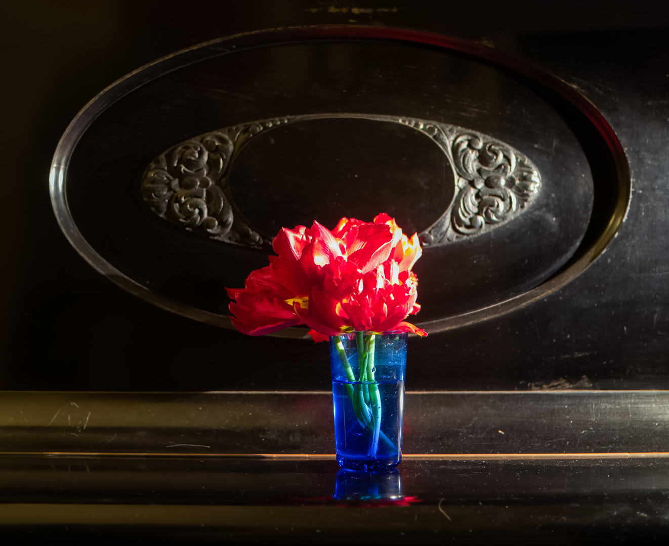 rote Tulpen im blauen Glas auf altem Klavier