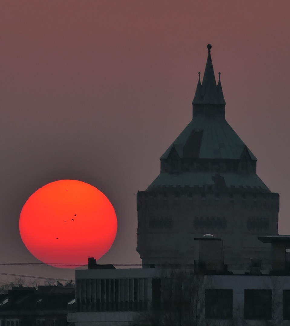 Roter Sonnenball durch viel Dunst geht neben dem Wasserturm unter