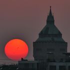 Roter Sonnenball durch viel Dunst geht neben dem Wasserturm unter