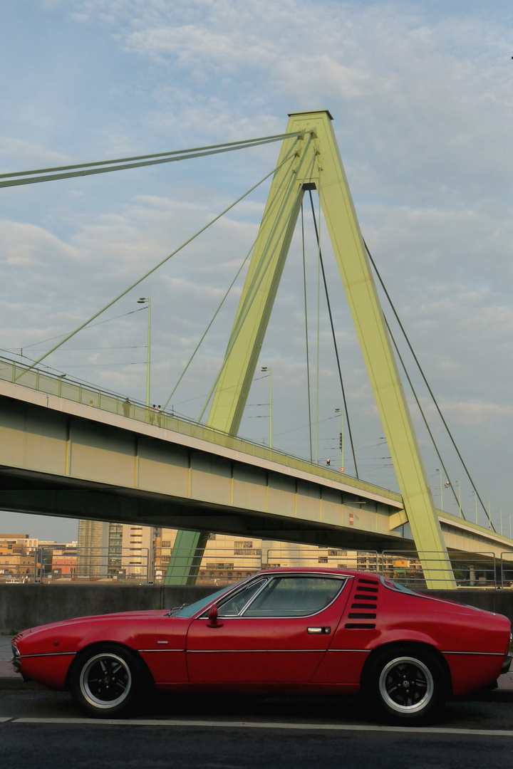 Roter Sportwagen vor grüner Brücke
