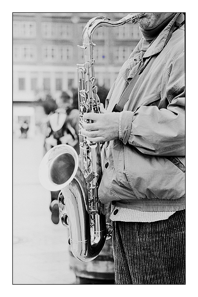 Saxophonspieler steht im Vordergrund anders der blaue Schirm hinten wegen Unschärfe kaum sichtbar