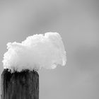 Schnee auf Holzpfosten vor verschneiter Landschaft