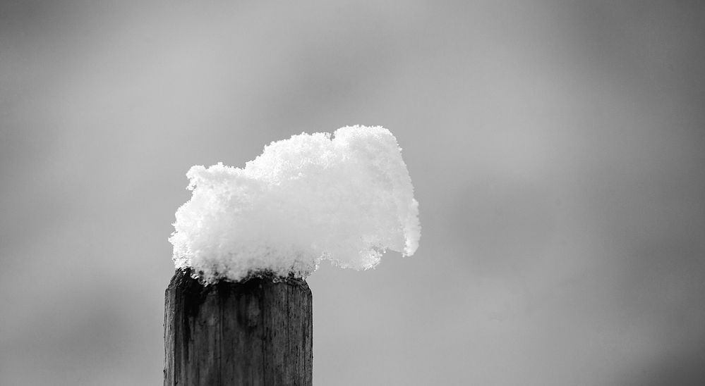 Schnee auf Holzpfosten vor verschneiter Landschaft