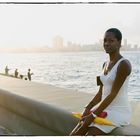 Schönheit sitzend am Malecon zu Havanna, mit zwei (2) Sonnenschirmen und ihrem Handy im Ausschnitt