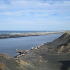 Schwarzer Sandstrand mit Treibholz am Flussufer bei Koitaita