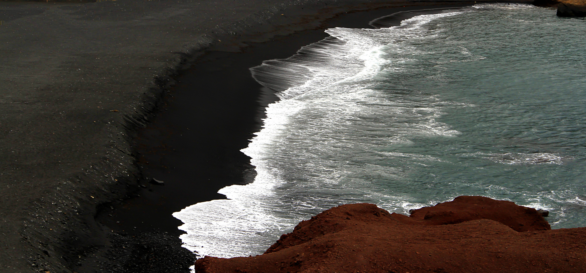 Schwarzer Strand und weisse Gischt