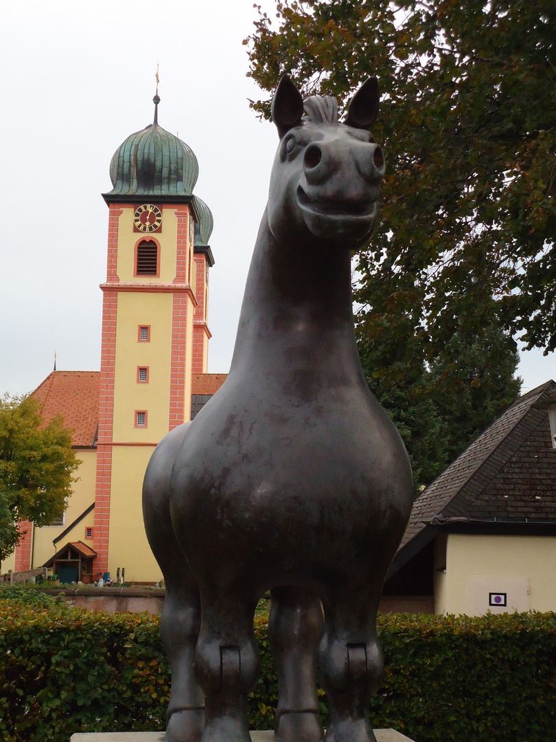 schwarzes Ross vor rot-gelber Kirche