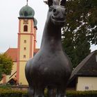 schwarzes Ross vor rot-gelber Kirche