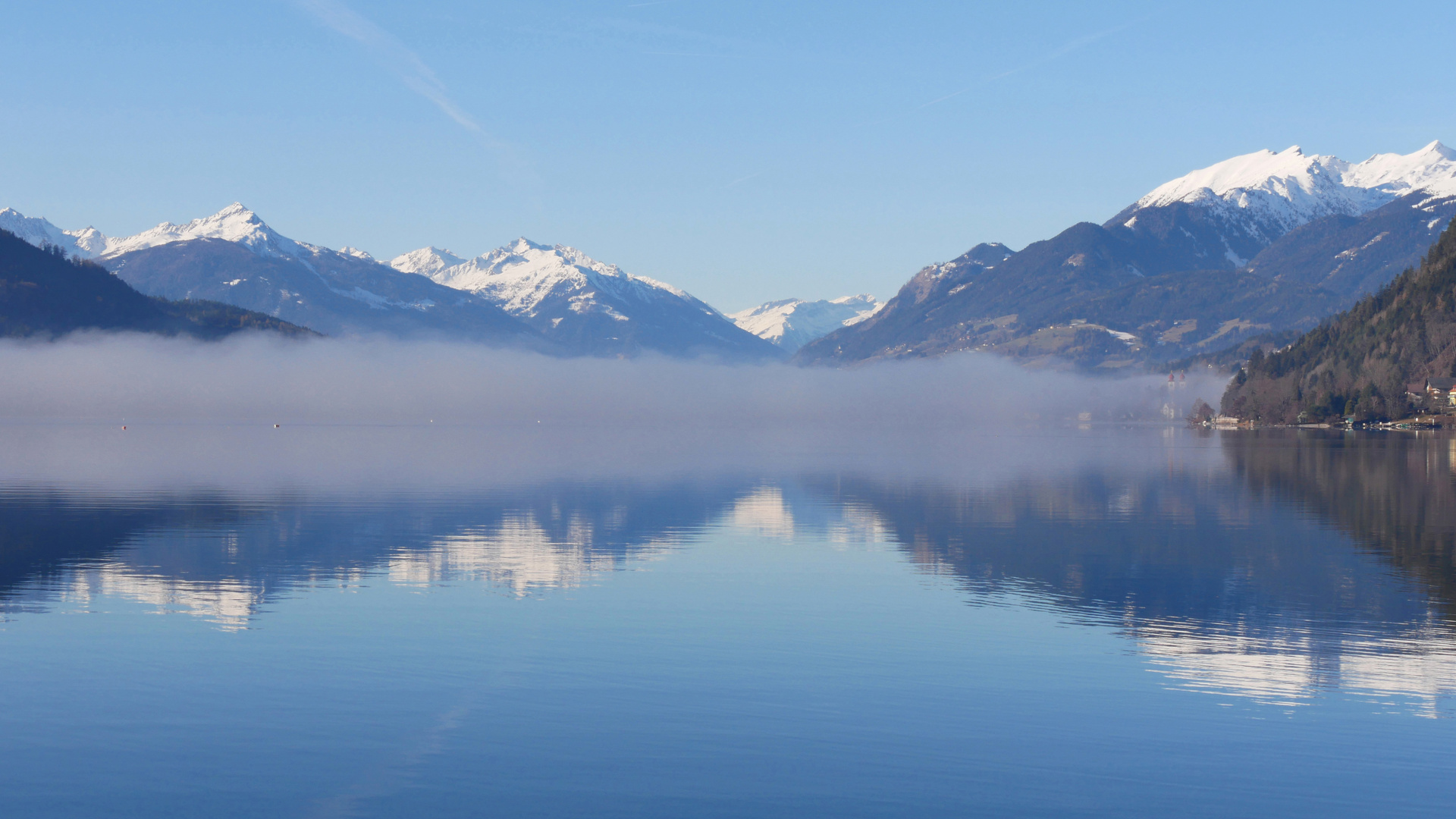 See mit Nebelbank und verschneiten Bergspitzen