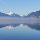 See mit Nebelbank und verschneiten Bergspitzen