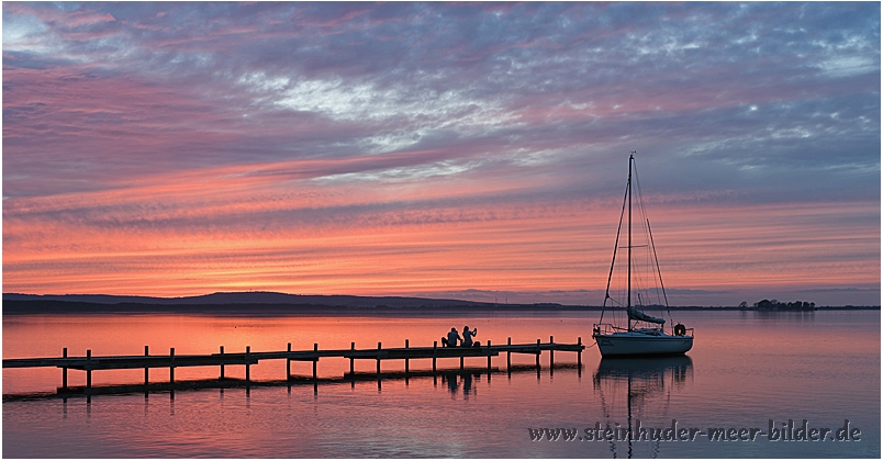 Silhouette von Paar mit Segelyacht bei Abendrot am Steg auf dem Steinhuder Meer bei Steinhude