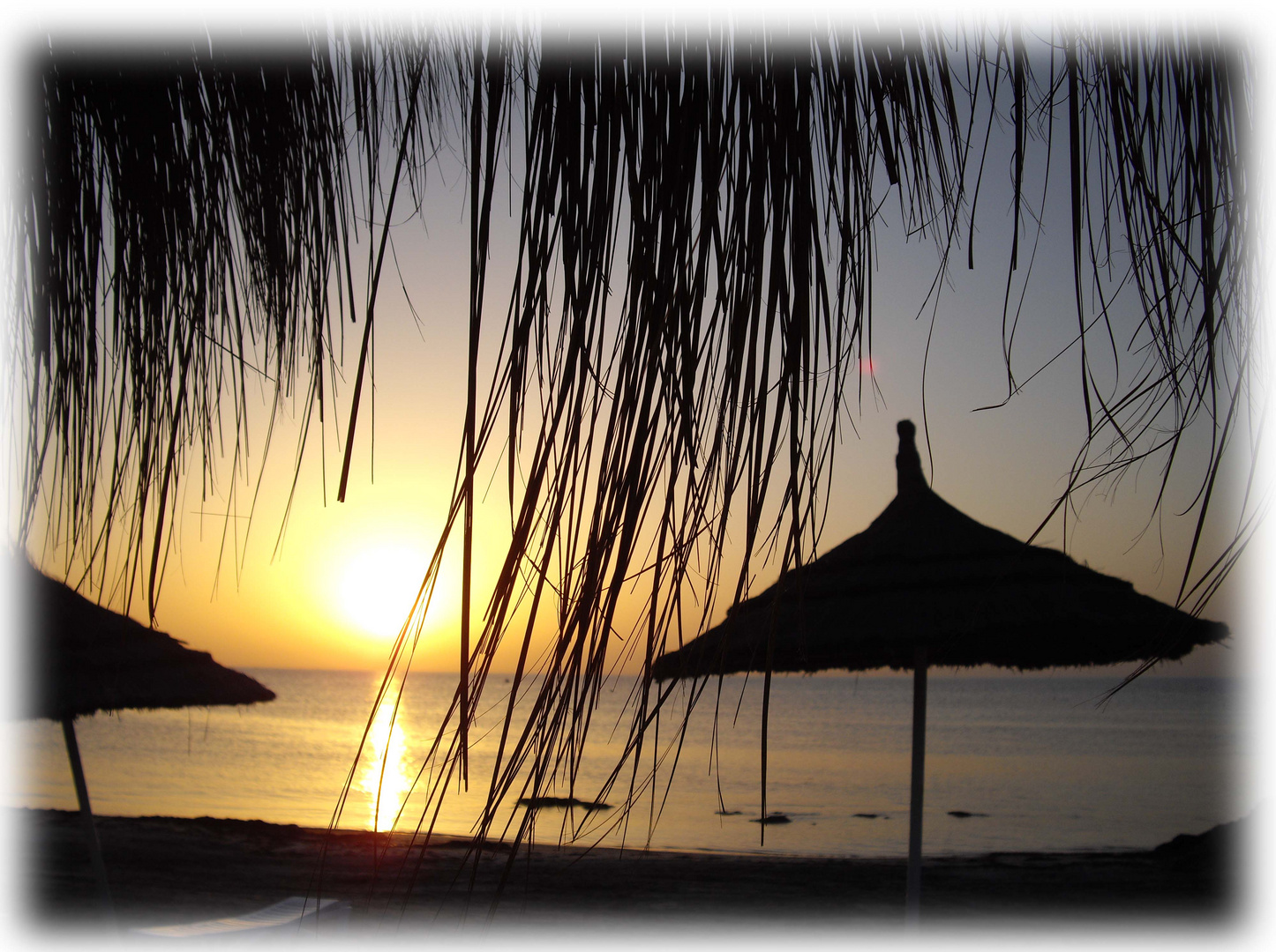 Sonnenaufgang auf Djerba mit Blick durch den Strohschirm