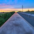 Spieglung des Abendrot auf dem Handlauf eines Brückengeländers.