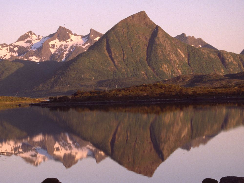 Spitze Berge spiegeln sich bei Sonnenschein auf den Lofoten