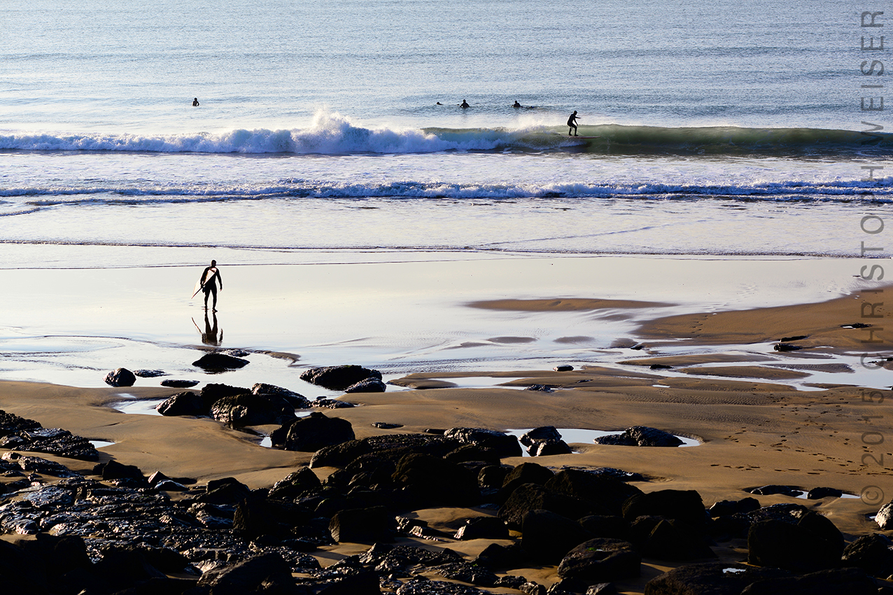 Strand mit Wellenreitern im Gegenlicht, Ireland