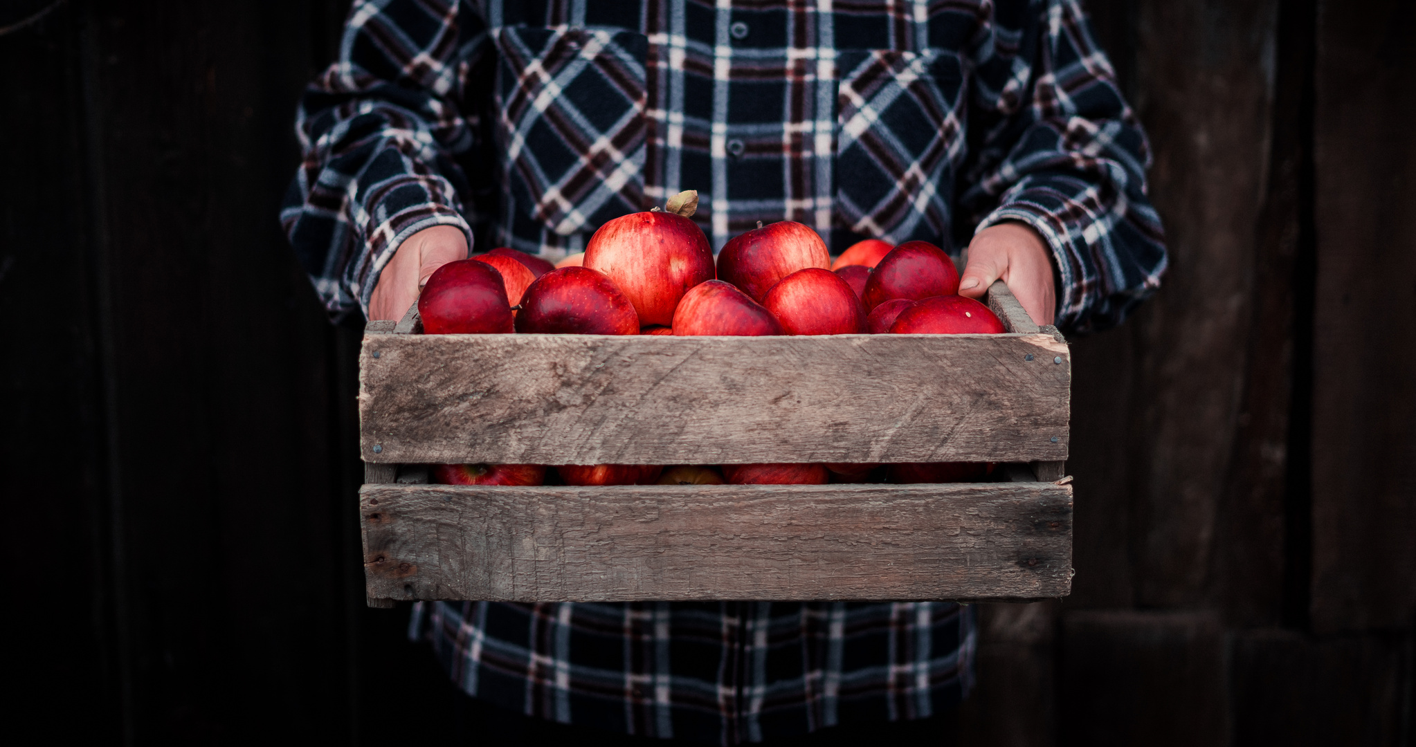 the woman is holding a wooden box with red apples