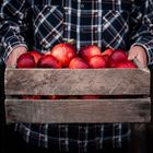 the woman is holding a wooden box with red apples