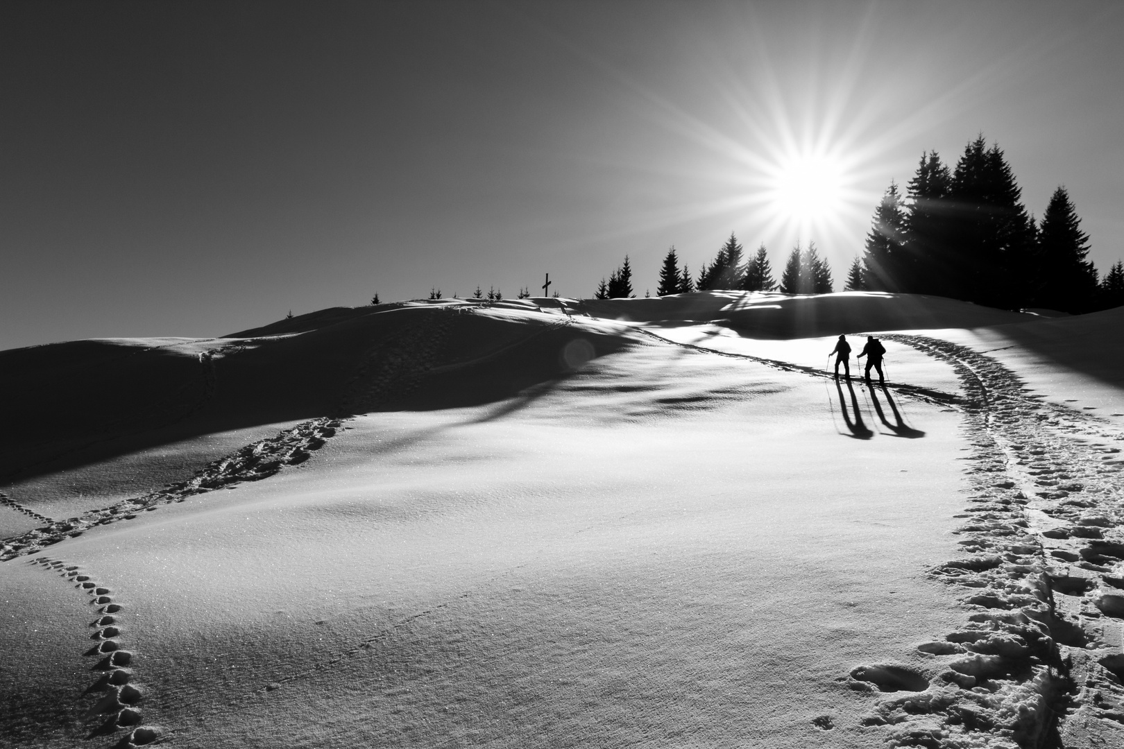 Two ski hikers walking towards summit cross. Sunbeams and backlight.