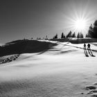 Two ski hikers walking towards summit cross. Sunbeams and backlight.