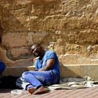 um Almosen Ersuchender Afrikaner an einer mediterranen Kirchenmauer