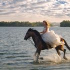 Une fille sur un cheval au galop le long du fleuve.