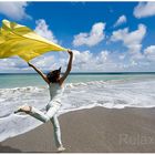 "Urlaubsgefühle" - Junge Frau mit wehendem gelbem Tuch läuft über Sandstrand am Meer