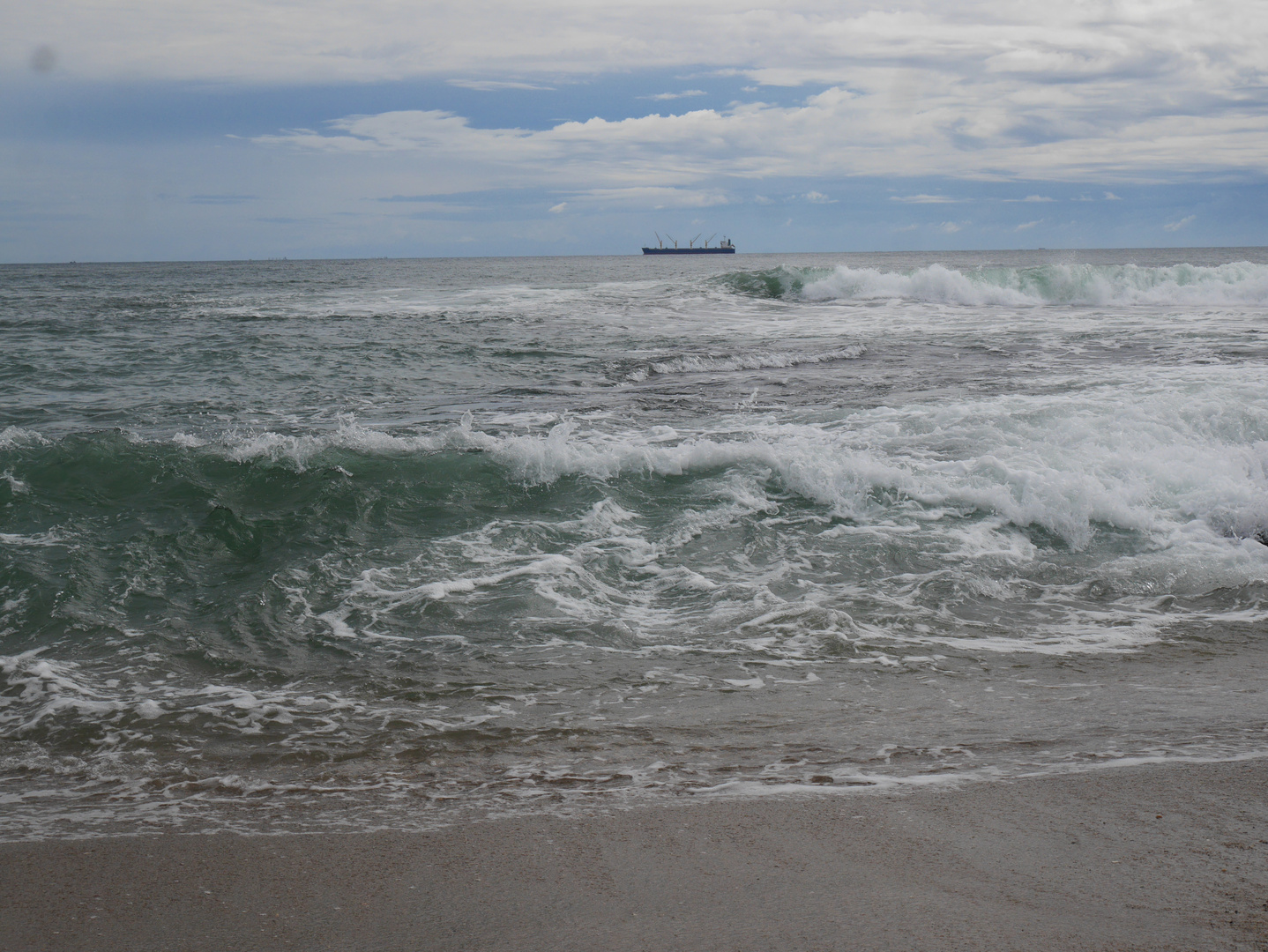 Wellen am Strand mit Schiff am Horizont