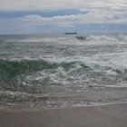 Wellen am Strand mit Schiff am Horizont