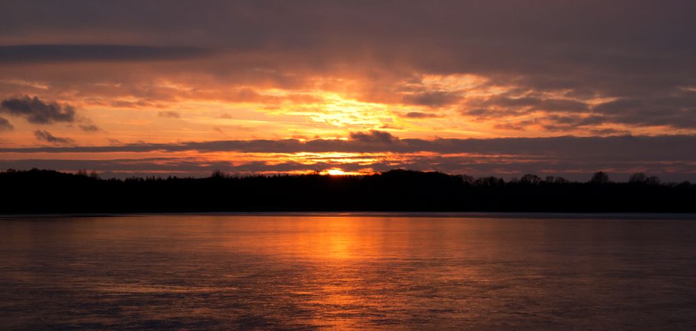 Winterlicher Sonnenuntergang über einem gefrorenen See