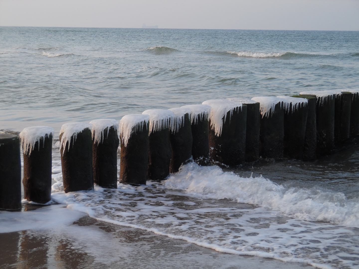 Wintersonne an Eiszapfen an Pfählen in der Ostsee