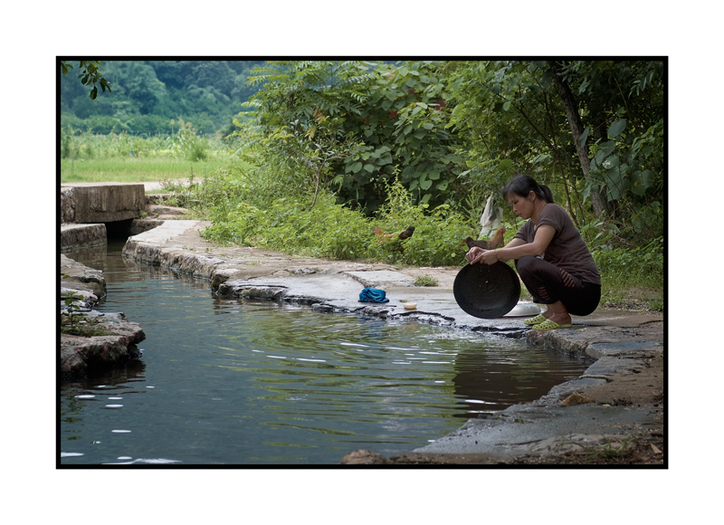 Woman washing dishes in a stream